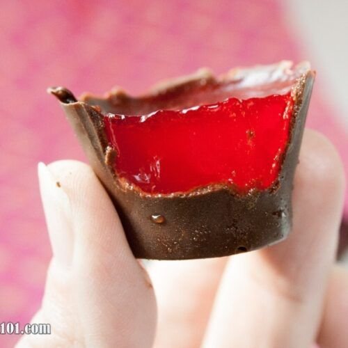 Chocolate-covered jello shot with red jello inside held by a hand.
