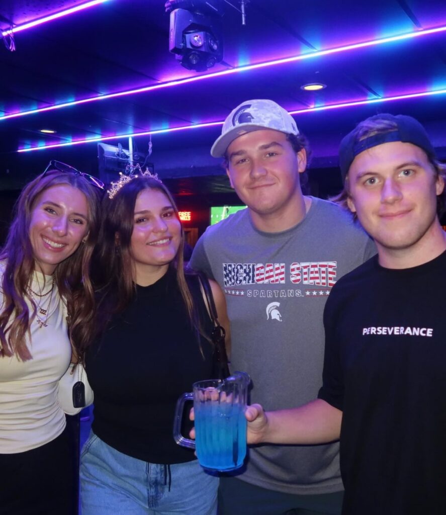 Four friends enjoying a karaoke night with drinks in a vibrant venue.