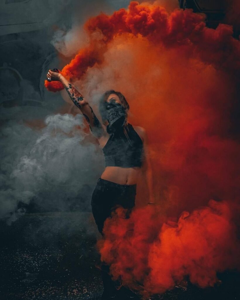 A person posing amidst thick, swirling clouds of vibrant orange and white smoke.