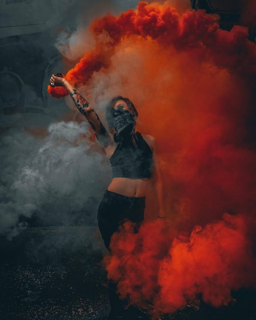 A person posing amidst thick, swirling clouds of vibrant orange and white smoke.