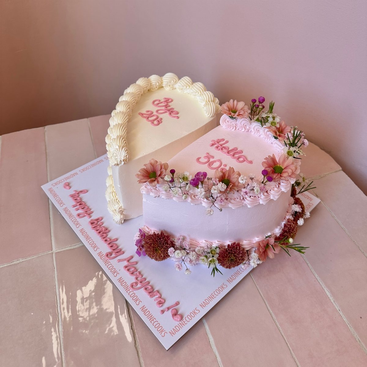 A heart-shaped pink and white birthday cake decorated with small pink and purple flowers.