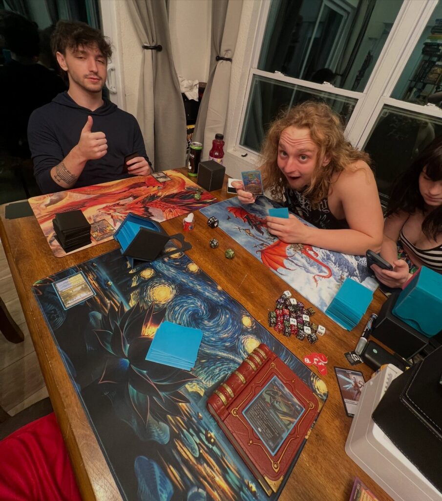 Young adults playing a trading card game with mats and dice on a wooden table.