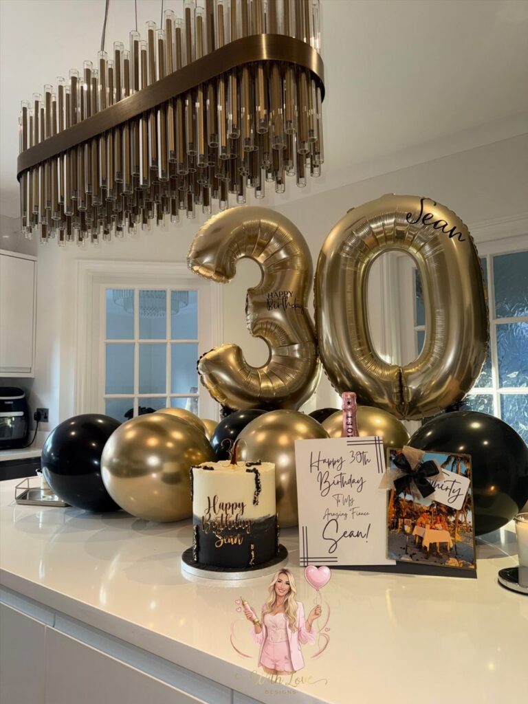 Gold number 30 balloons and a birthday cake on a white kitchen counter.