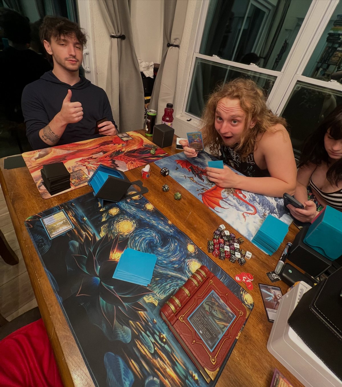 Young adults playing a trading card game with mats and dice on a wooden table.