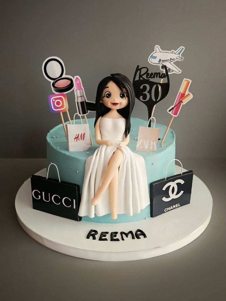 A light blue birthday cake featuring a fondant woman, makeup toppers, and luxury brand shopping bags.
