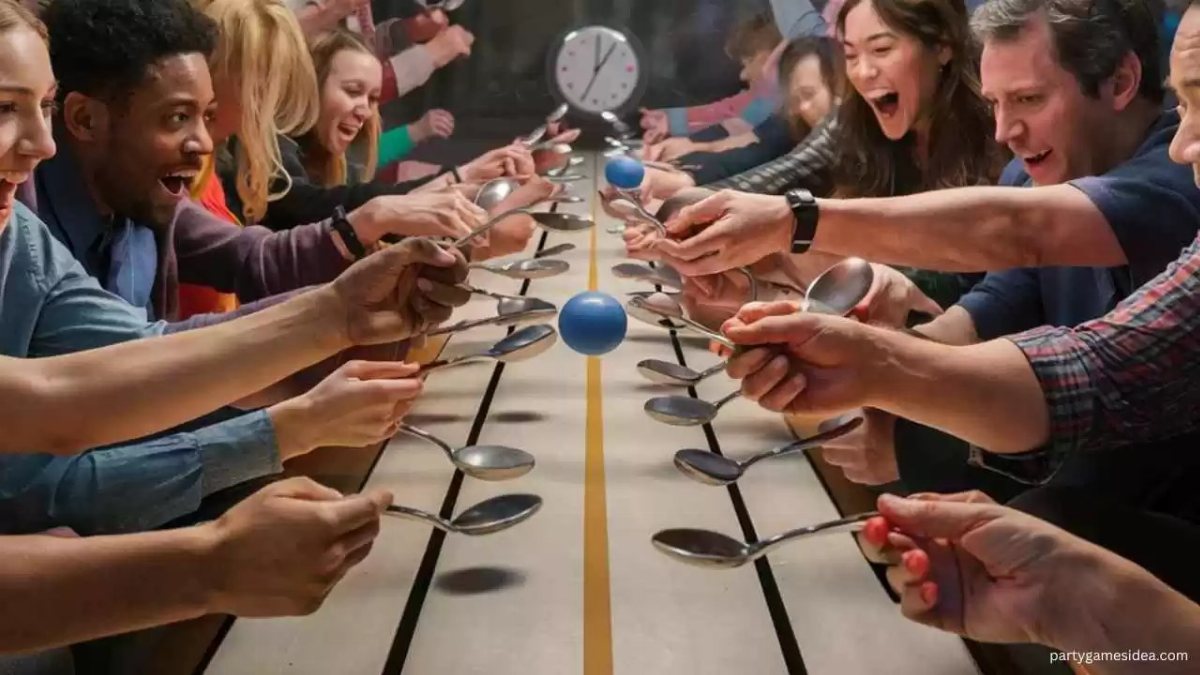 People using spoons to balance blue ping pong balls on a long table during a game.