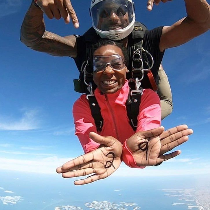 A person in a pink shirt skydiving while showing the number 30 on their palms.