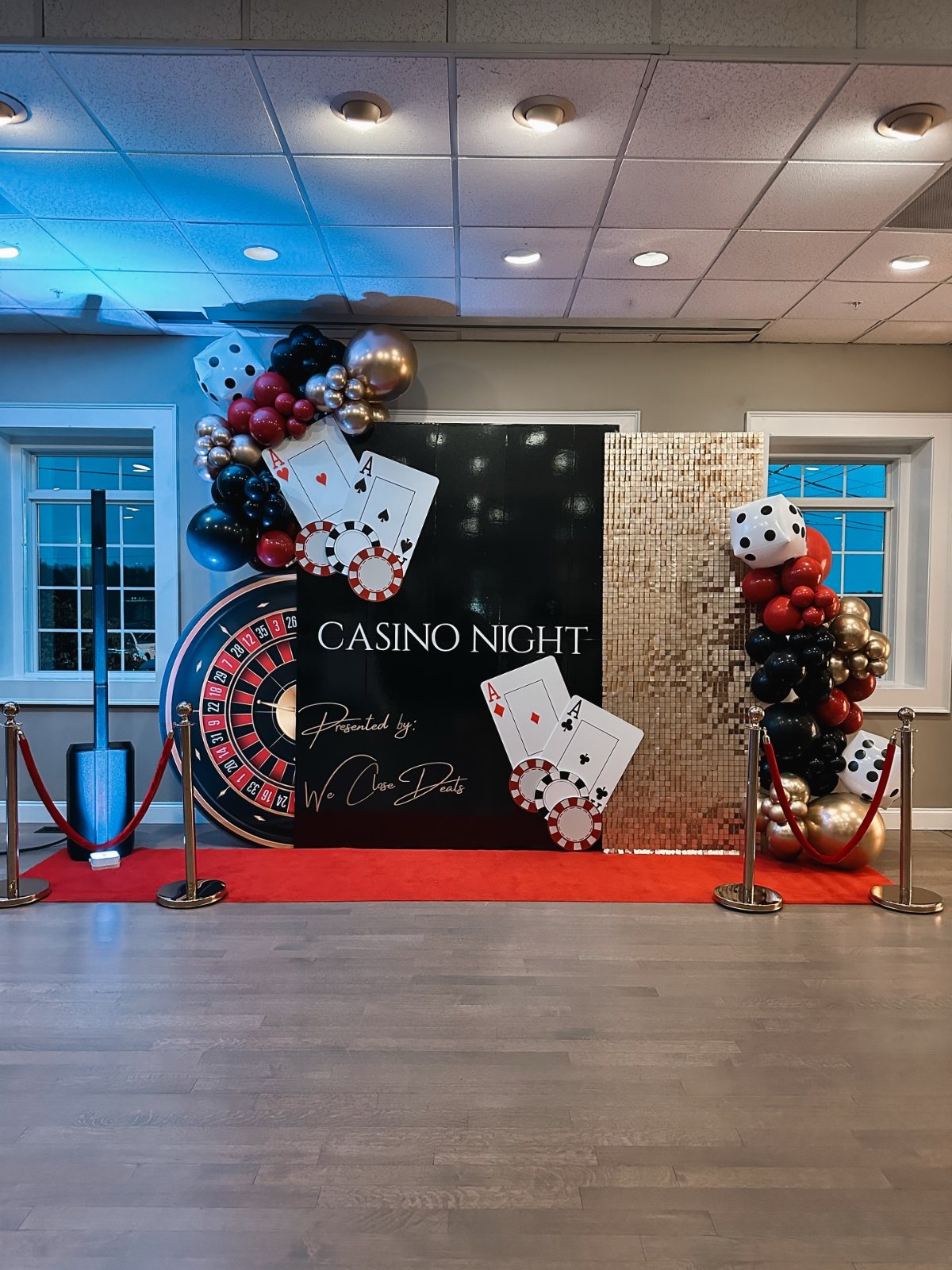 Casino night party backdrop with balloons, playing cards, dice, and a large roulette wheel.