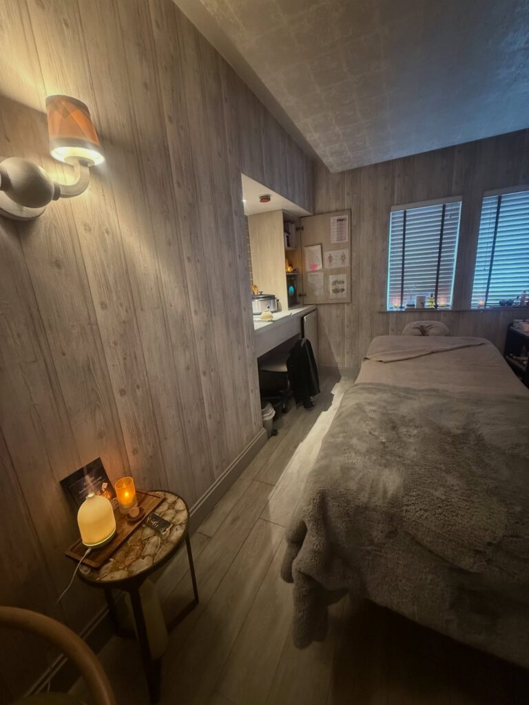 A massage table with a grey faux-fur blanket in a dimly lit room with wood-paneled walls.
