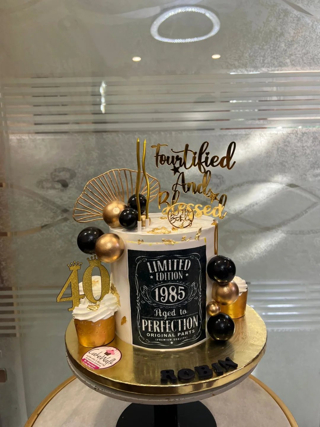 A white and gold 40th birthday cake decorated with black spheres and vintage 1985 themed signage.