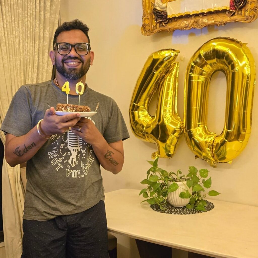 A man smiling while holding a birthday cake with a forty candle and gold balloons.