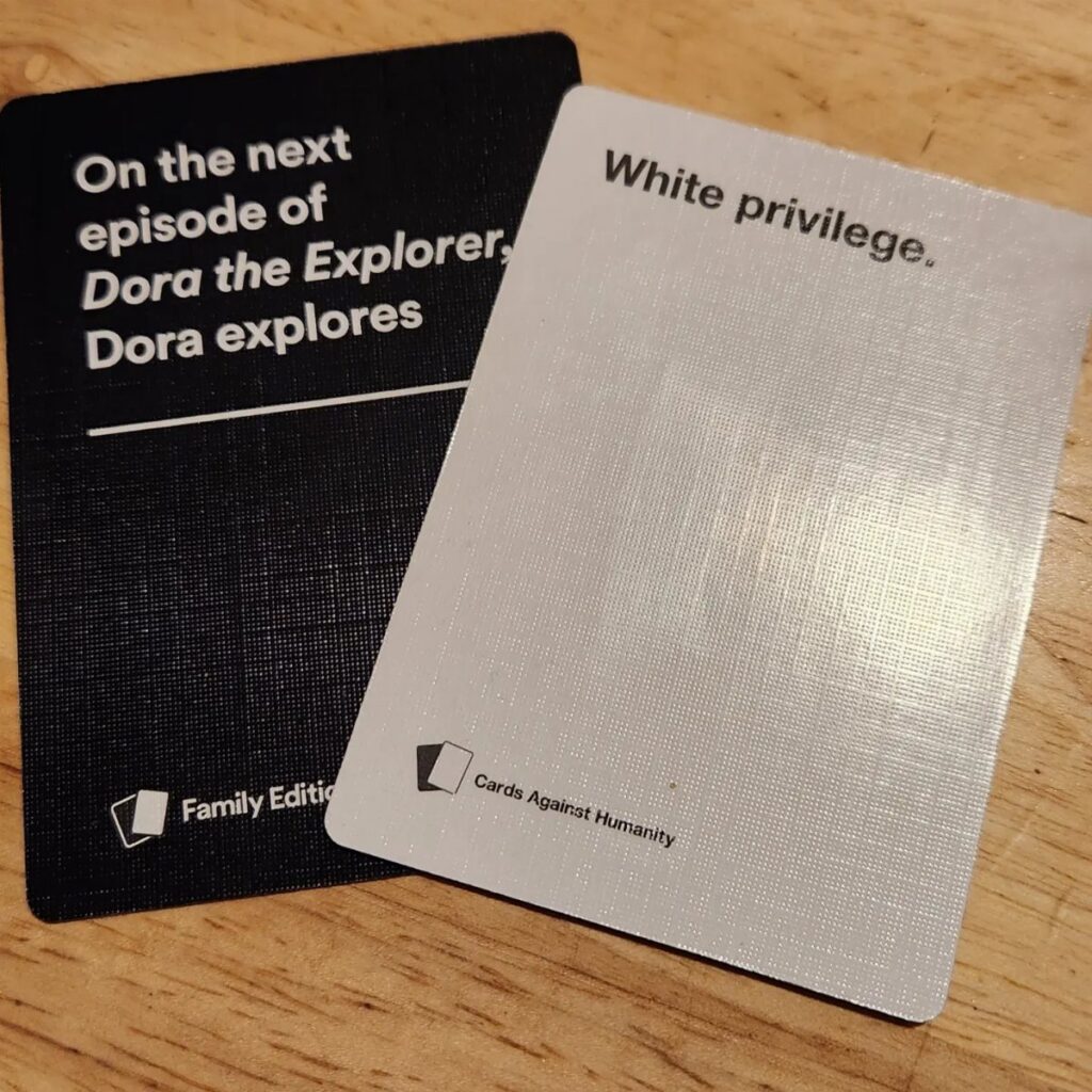 Two Cards Against Humanity cards resting on a light brown wooden table surface.