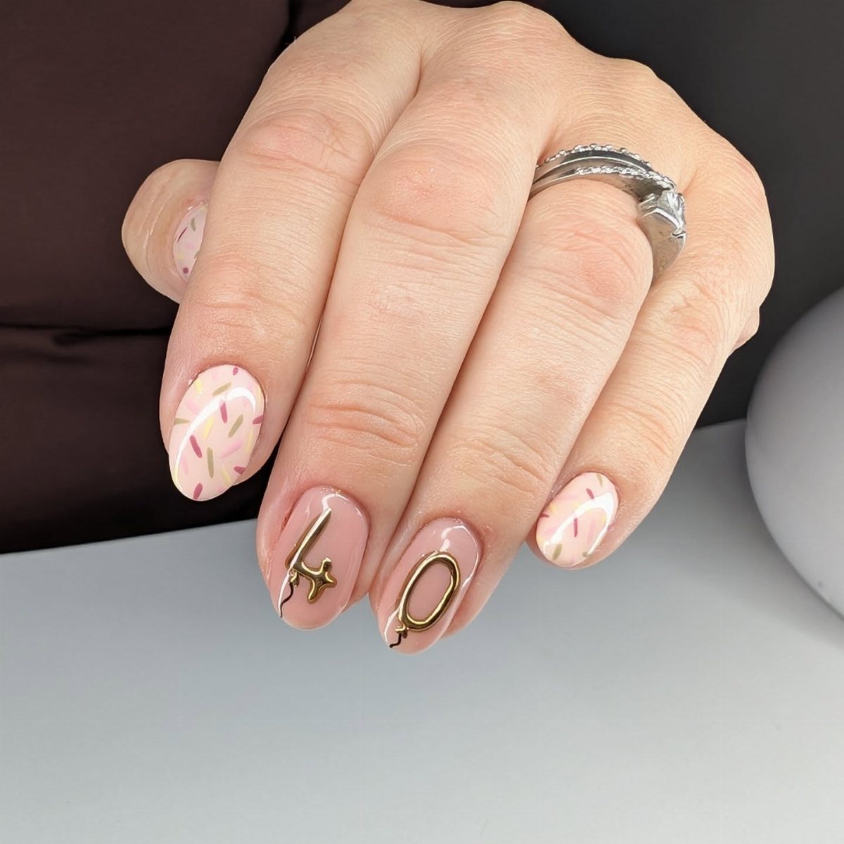 Manicured hand with confetti pattern nails and gold number forty nail art.