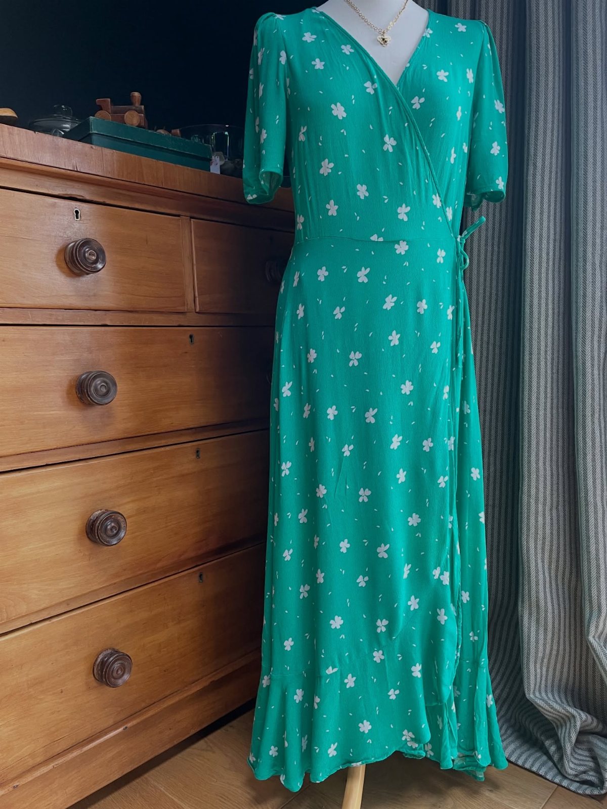 Green floral wrap dress displayed on a mannequin next to a wooden dresser.