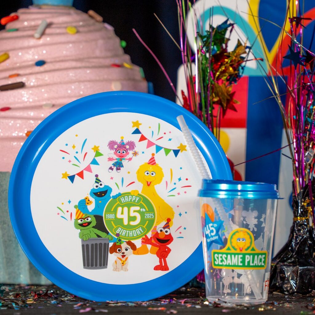 Blue Sesame Street themed birthday plate and cup next to a pink frosted cake.