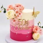 An ombre pink and cream cake decorated with roses and gold fabulous fifty lettering.