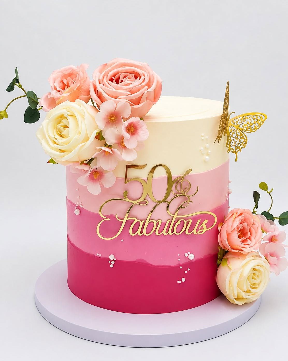 An ombre pink and cream cake decorated with roses and gold fabulous fifty lettering.