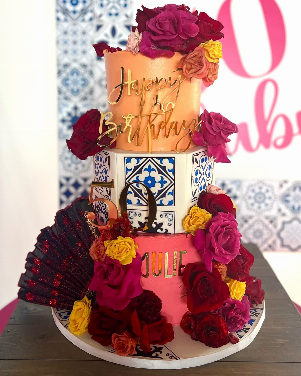 A three-tiered floral birthday cake featuring blue tile patterns and a gold number fifty.