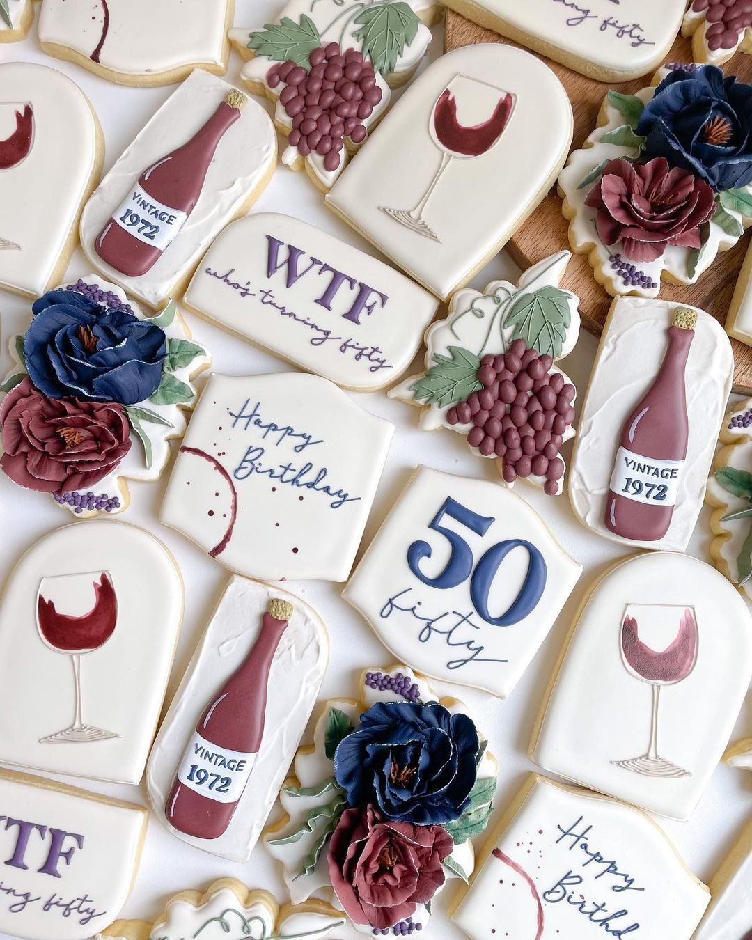 Decorated sugar cookies shaped like wine bottles, glasses, and flowers with fifty birthday text.