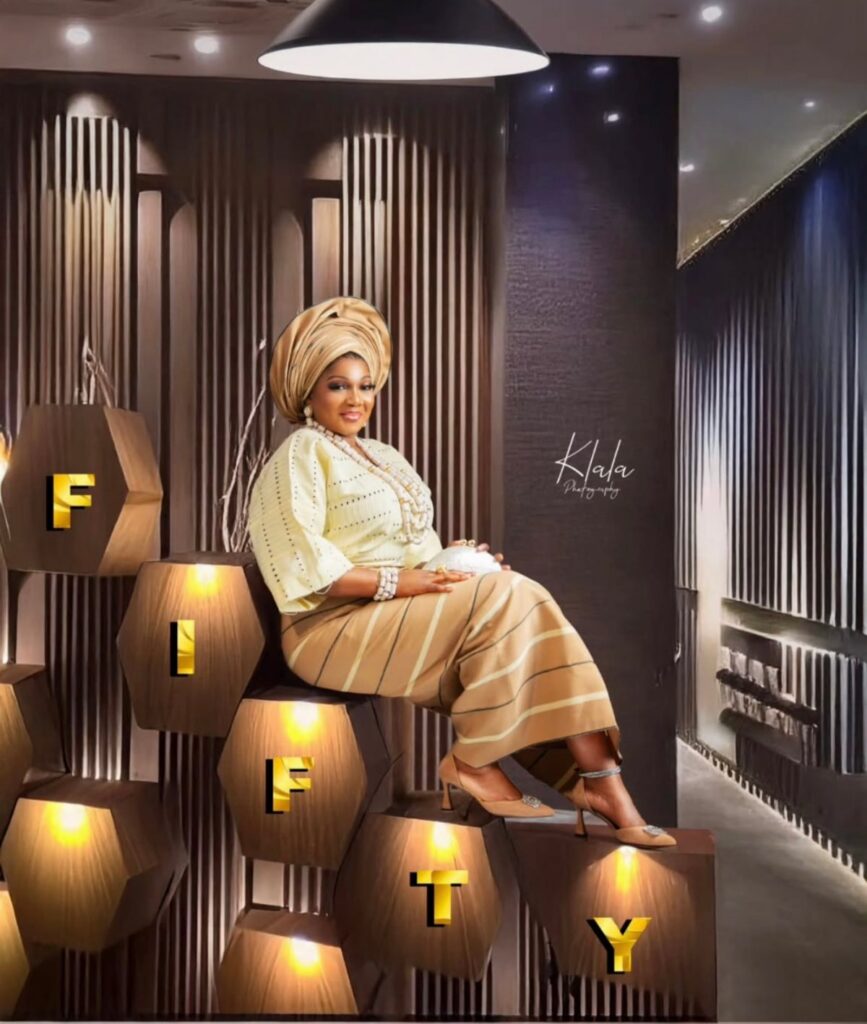 A woman in gold traditional attire sitting on large illuminated blocks spelling FIFTY.