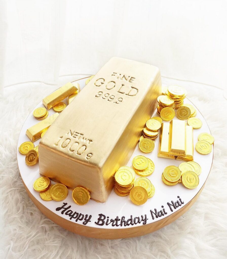 A gold bar shaped cake surrounded by gold coins and small gold bars on a white platter.