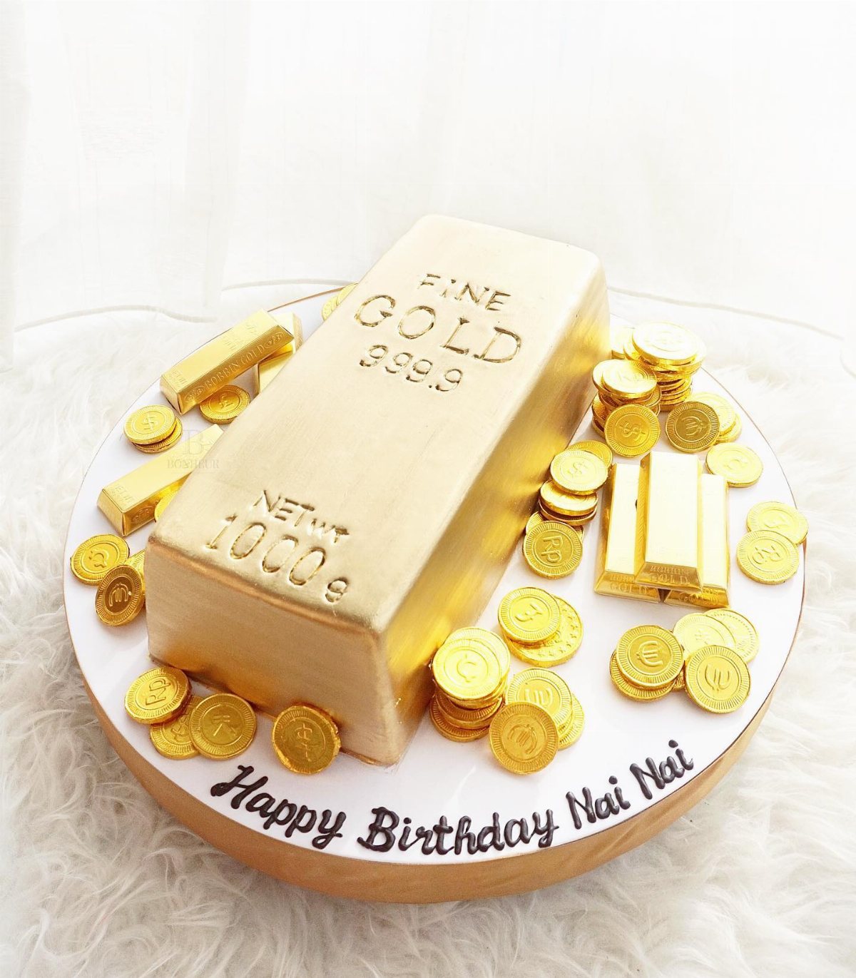 A gold bar shaped cake surrounded by gold coins and small gold bars on a white platter.