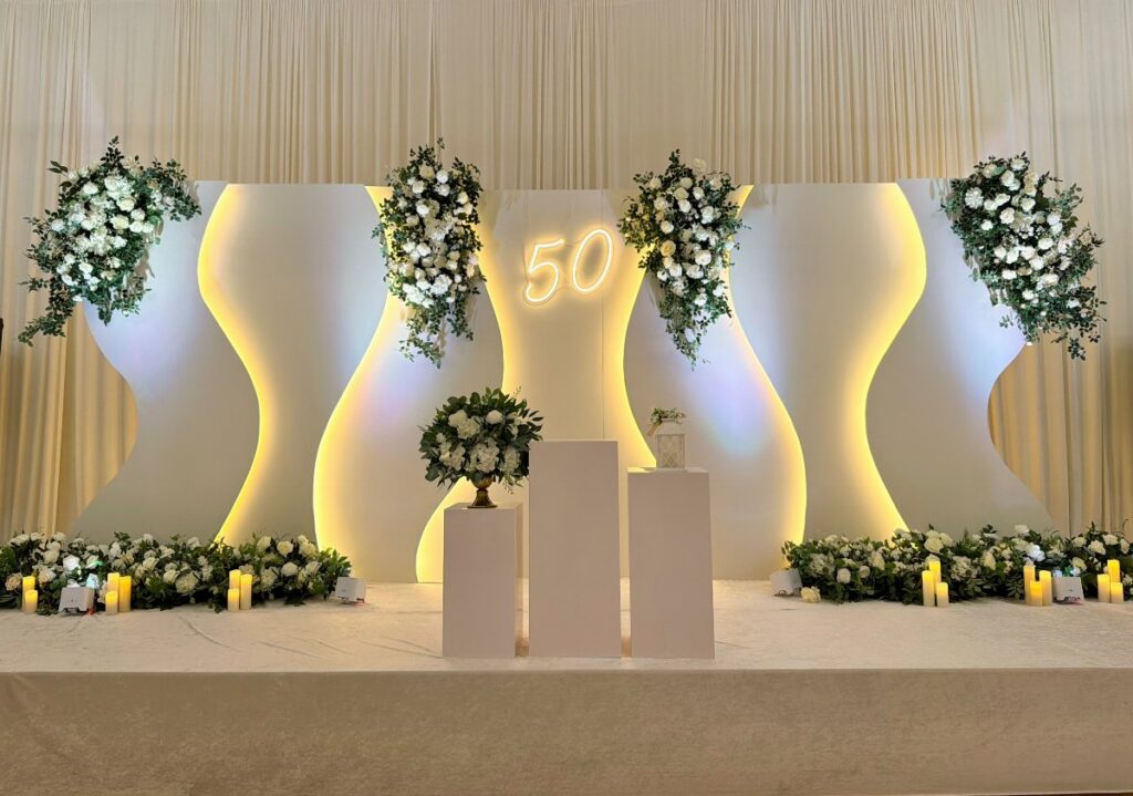 White wavy backdrop with glowing number 50 and white floral arrangements on a stage.