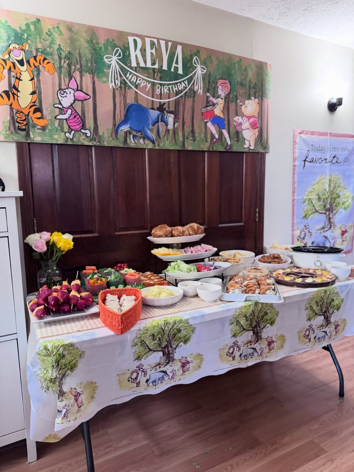 A buffet table filled with party food under a Winnie the Pooh themed birthday banner.