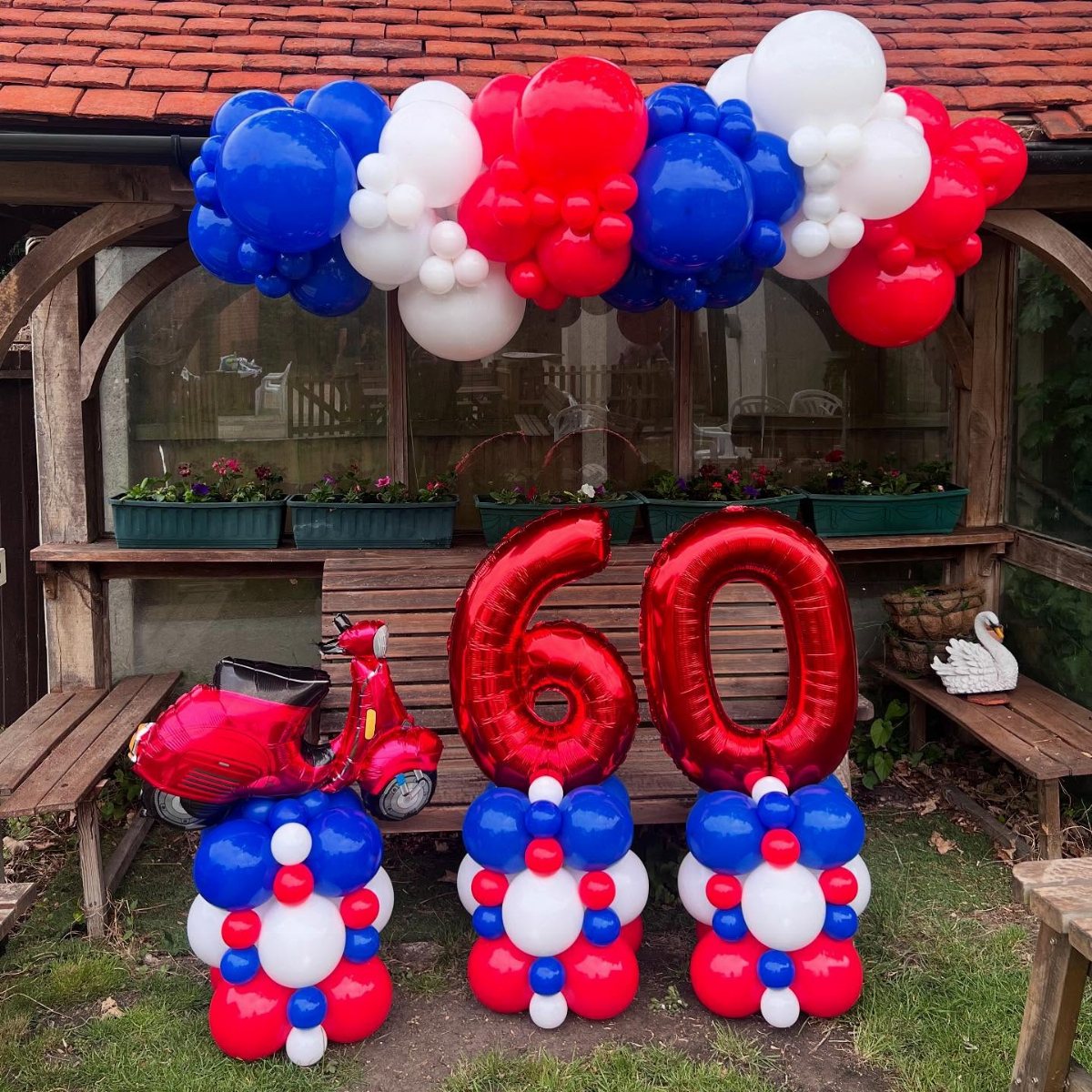 Red, white, and blue balloon decorations featuring large number sixty balloons and a red scooter balloon.