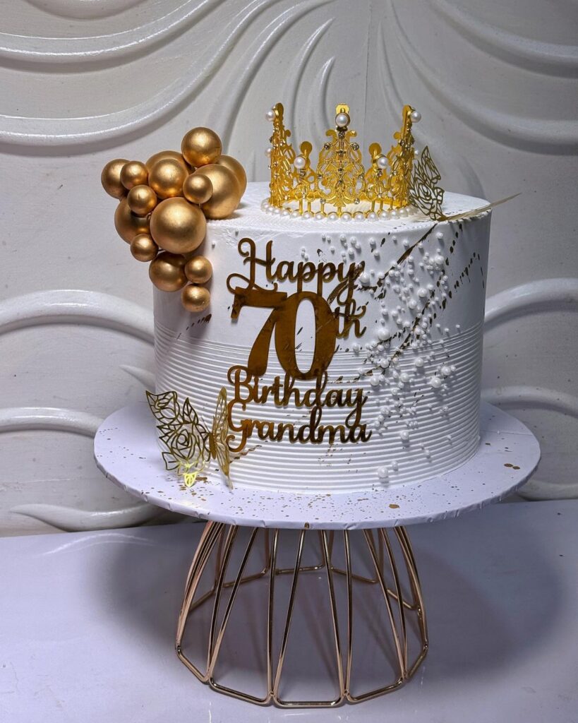 White textured cake with gold crown, gold spheres, and Happy 70th Birthday Grandma lettering.