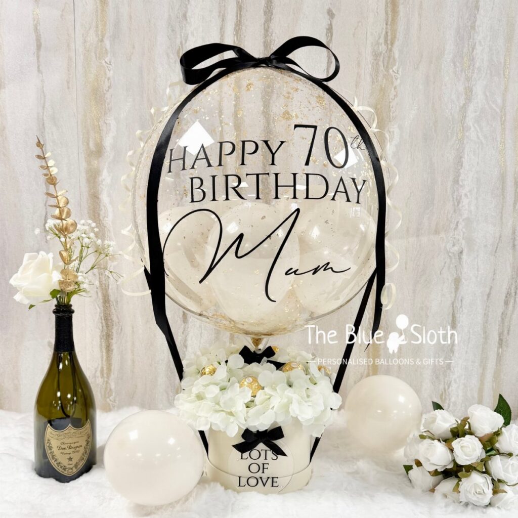 Large clear balloon with black text celebrating a 70th birthday surrounded by white flowers and balloons.