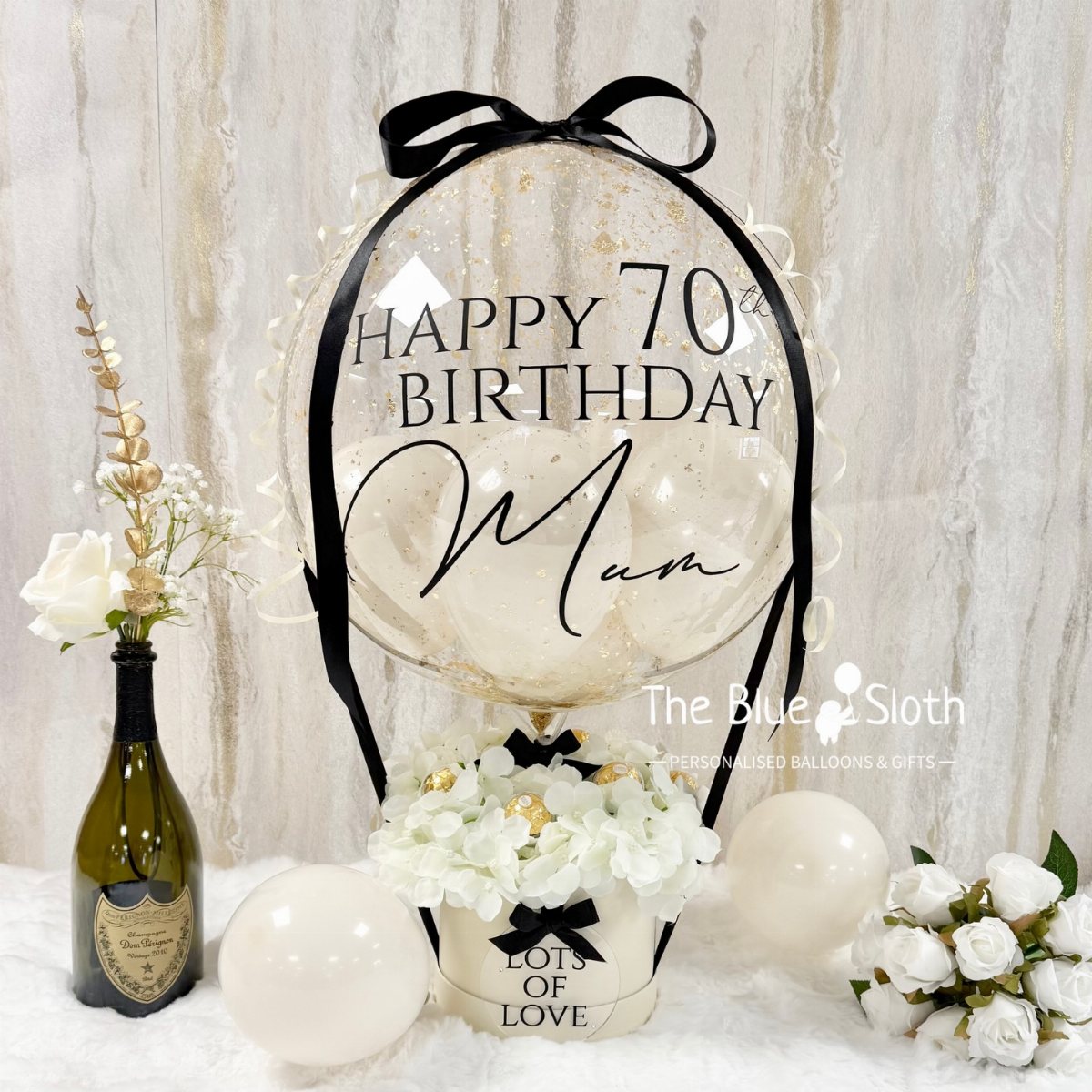Large clear balloon with black text celebrating a 70th birthday surrounded by white flowers and balloons.