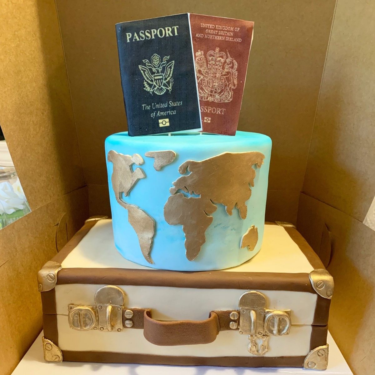 A travel-themed cake featuring a world map tier and edible passports atop a suitcase-shaped base.