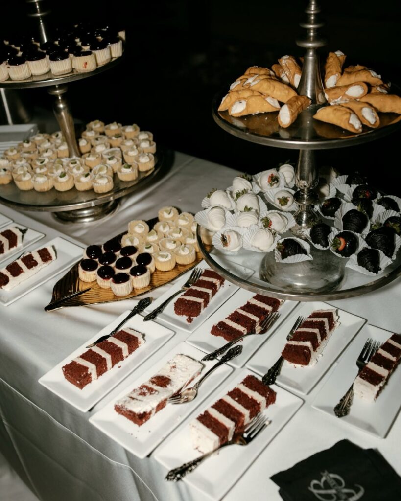 Assorted miniature desserts and red velvet cake slices arranged on silver stands and white plates.