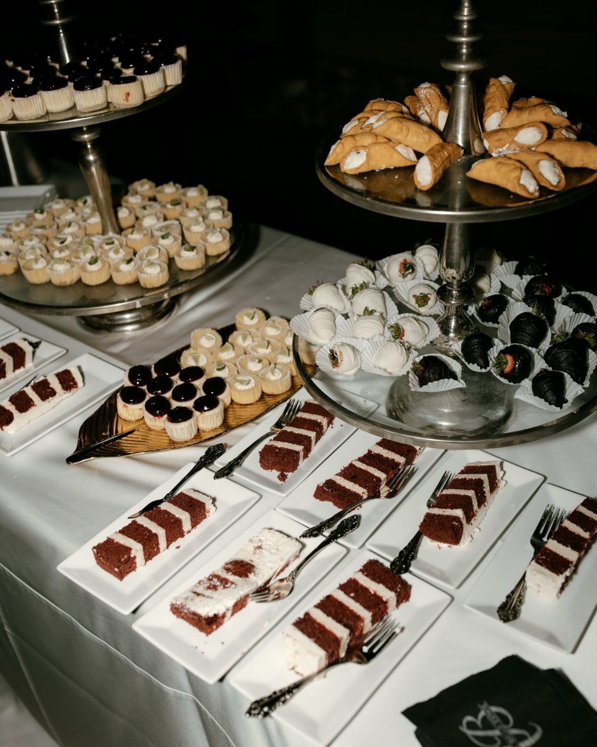Assorted miniature desserts and red velvet cake slices arranged on silver stands and white plates.