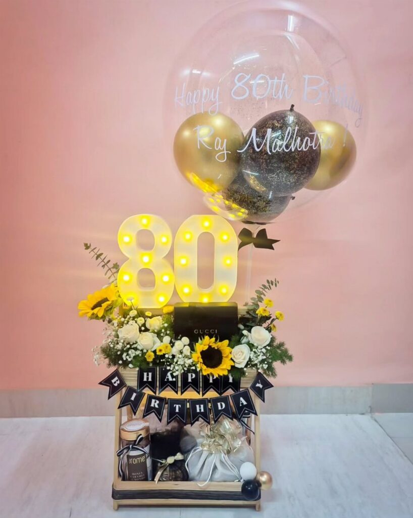 A celebratory gift basket featuring glowing number 80 lights, sunflowers, and balloons for an 80th birthday.