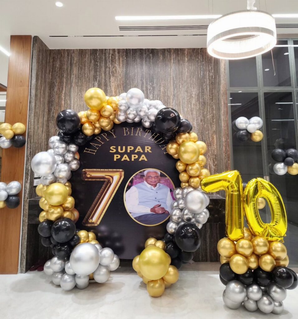 Birthday decorations with black, gold, and silver balloons surrounding a large 70th birthday backdrop.