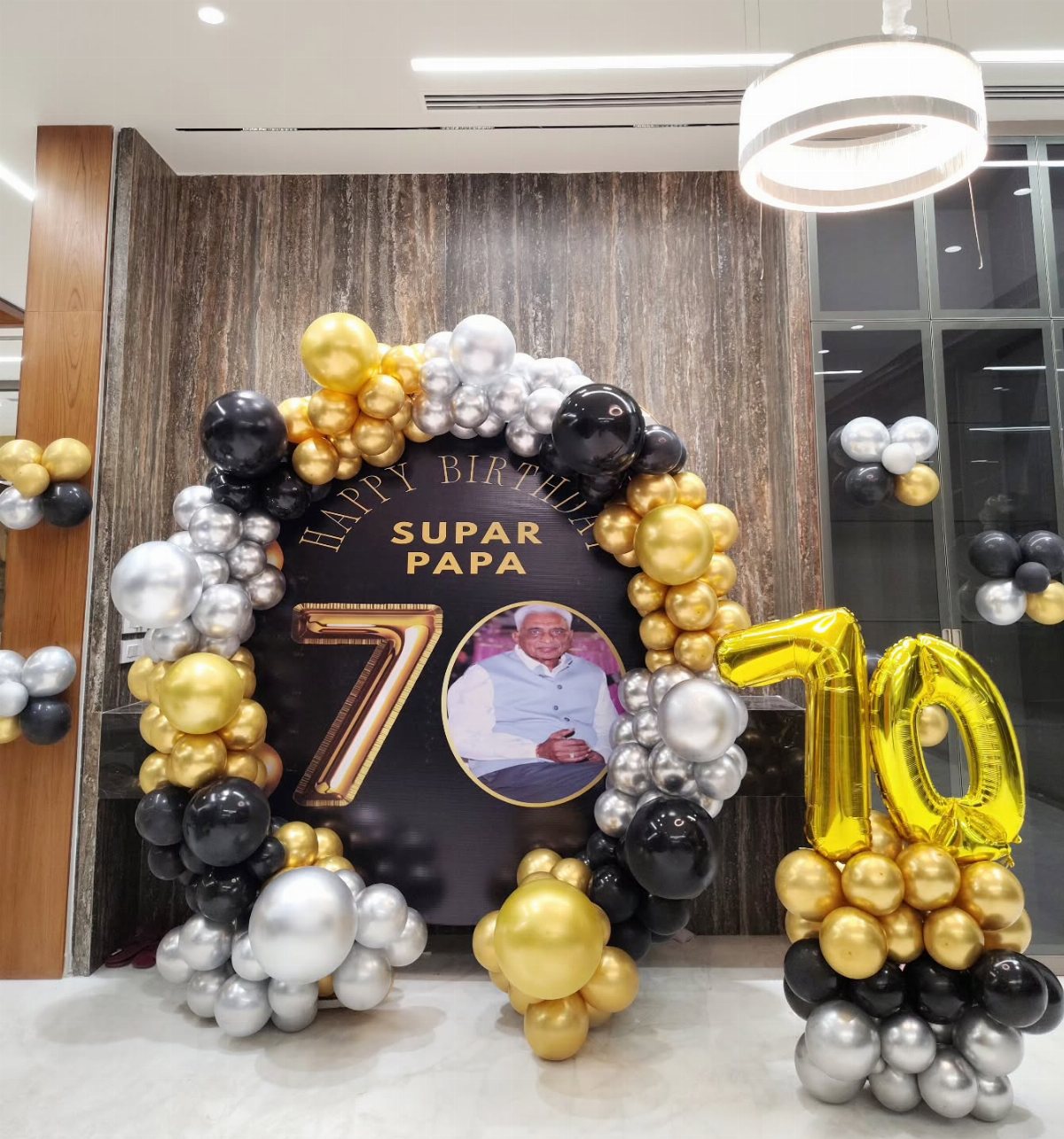 Birthday decorations with black, gold, and silver balloons surrounding a large 70th birthday backdrop.