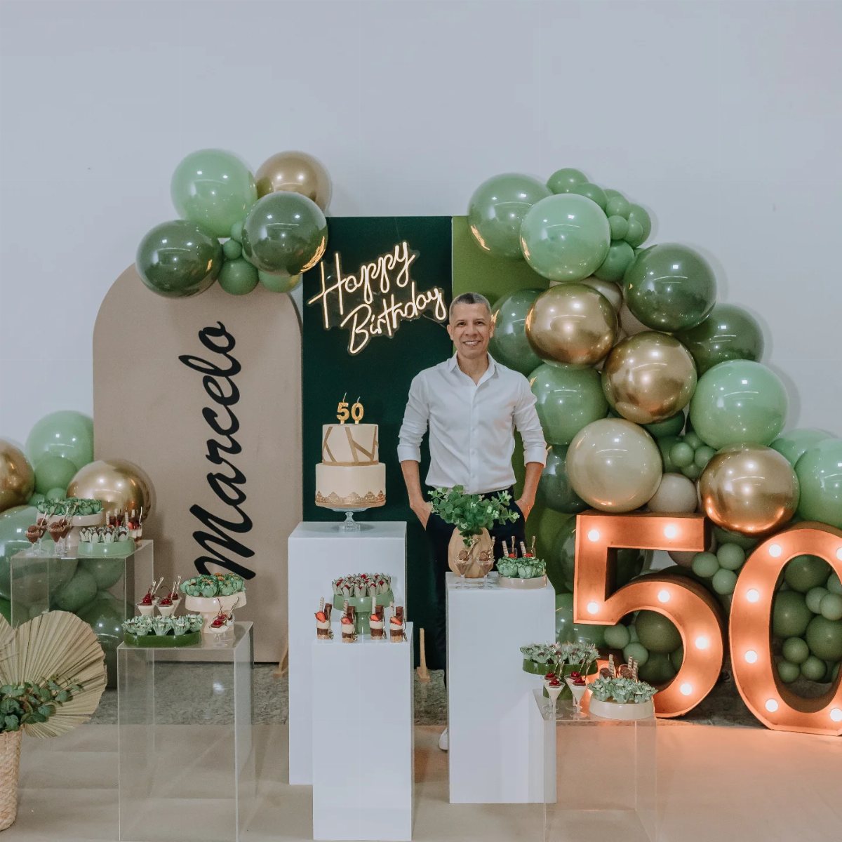 Man standing in front of a green and gold 50th birthday party decoration setup.