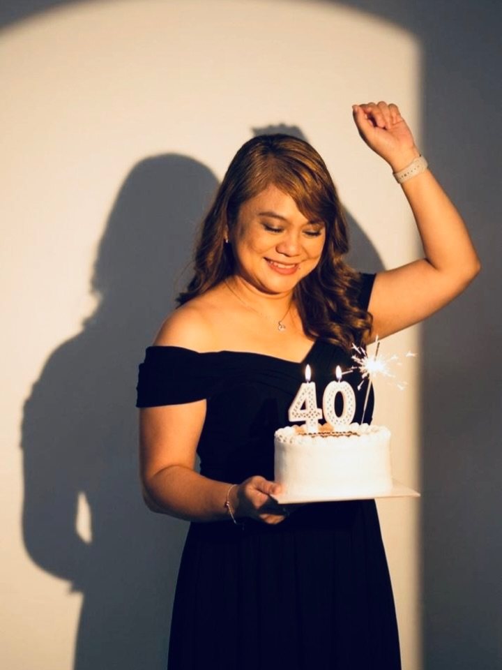 A woman in a black dress smiling while holding a birthday cake with a forty candle.