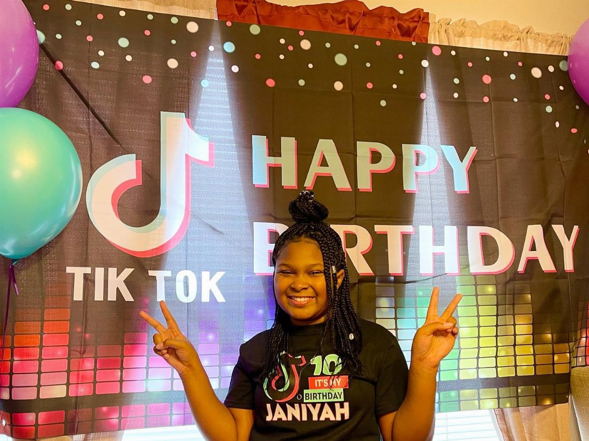 A smiling girl posing in front of a TikTok themed happy birthday backdrop.