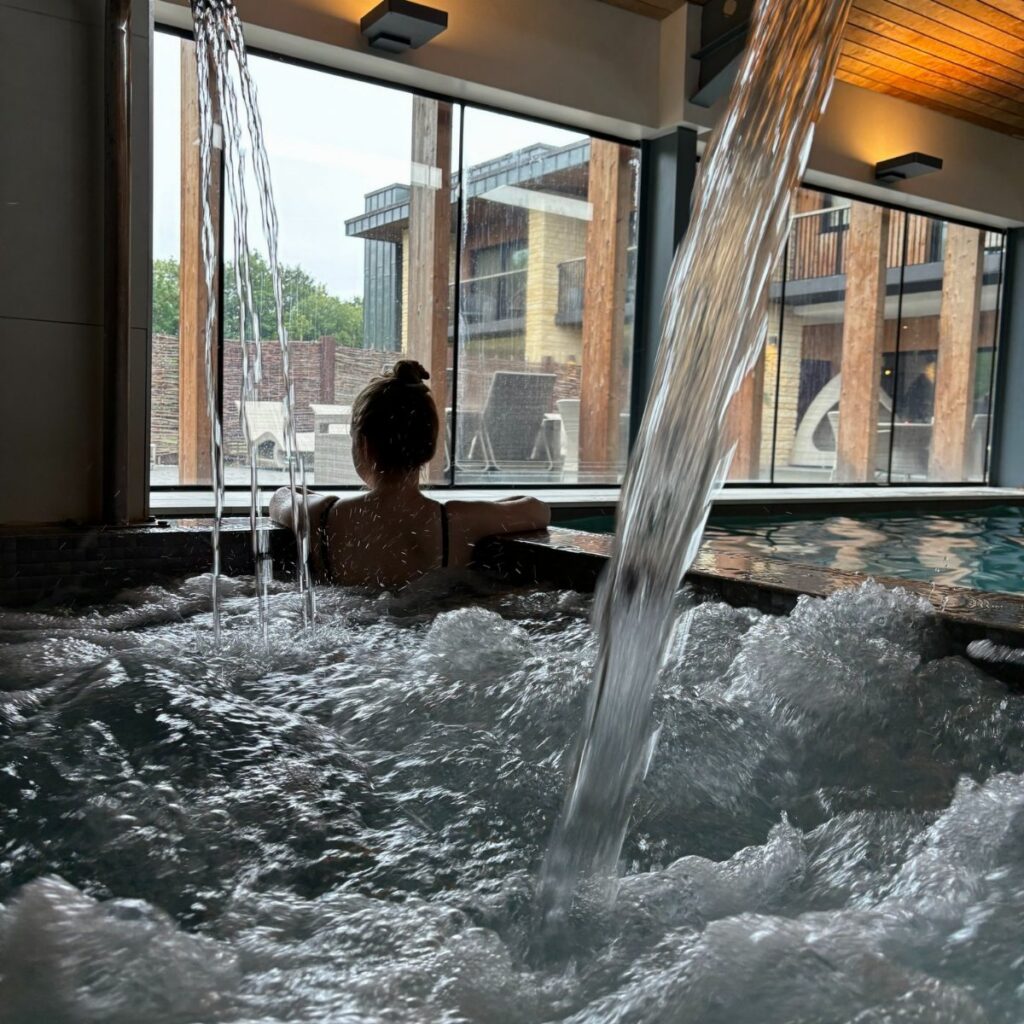 A person sitting in a bubbling indoor hot tub looking out through large windows.