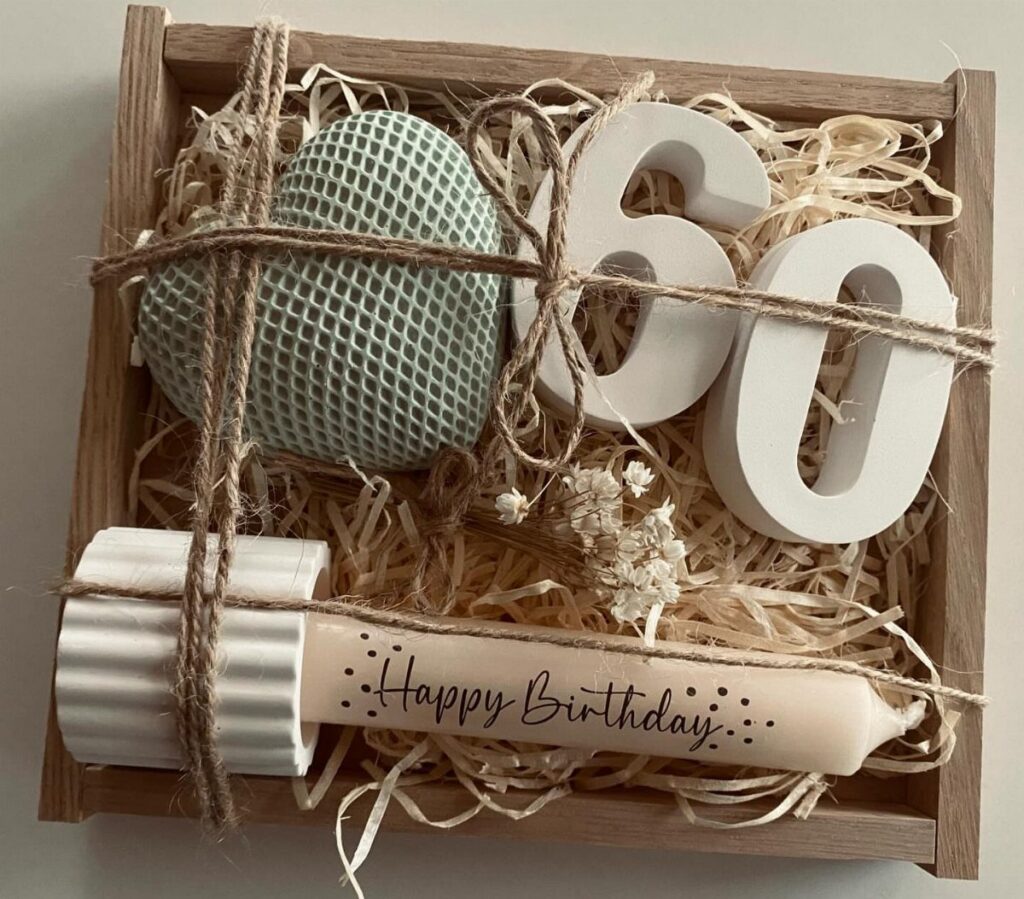 A wooden gift box containing a teal heart, white number sixty, and a happy birthday candle.