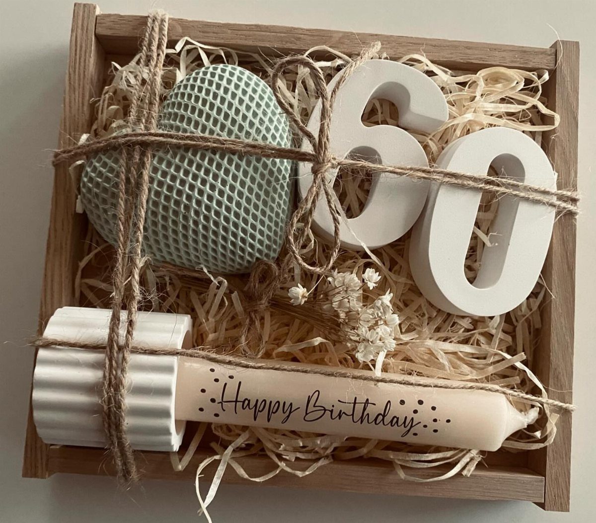 A wooden gift box containing a teal heart, white number sixty, and a happy birthday candle.