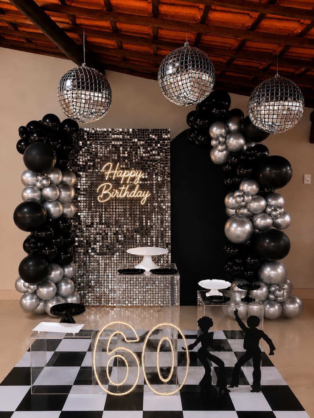Disco balls and black and silver balloons decorate a 60th birthday party setup.