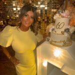 A woman in a yellow dress standing next to a decorated 60th birthday cake.