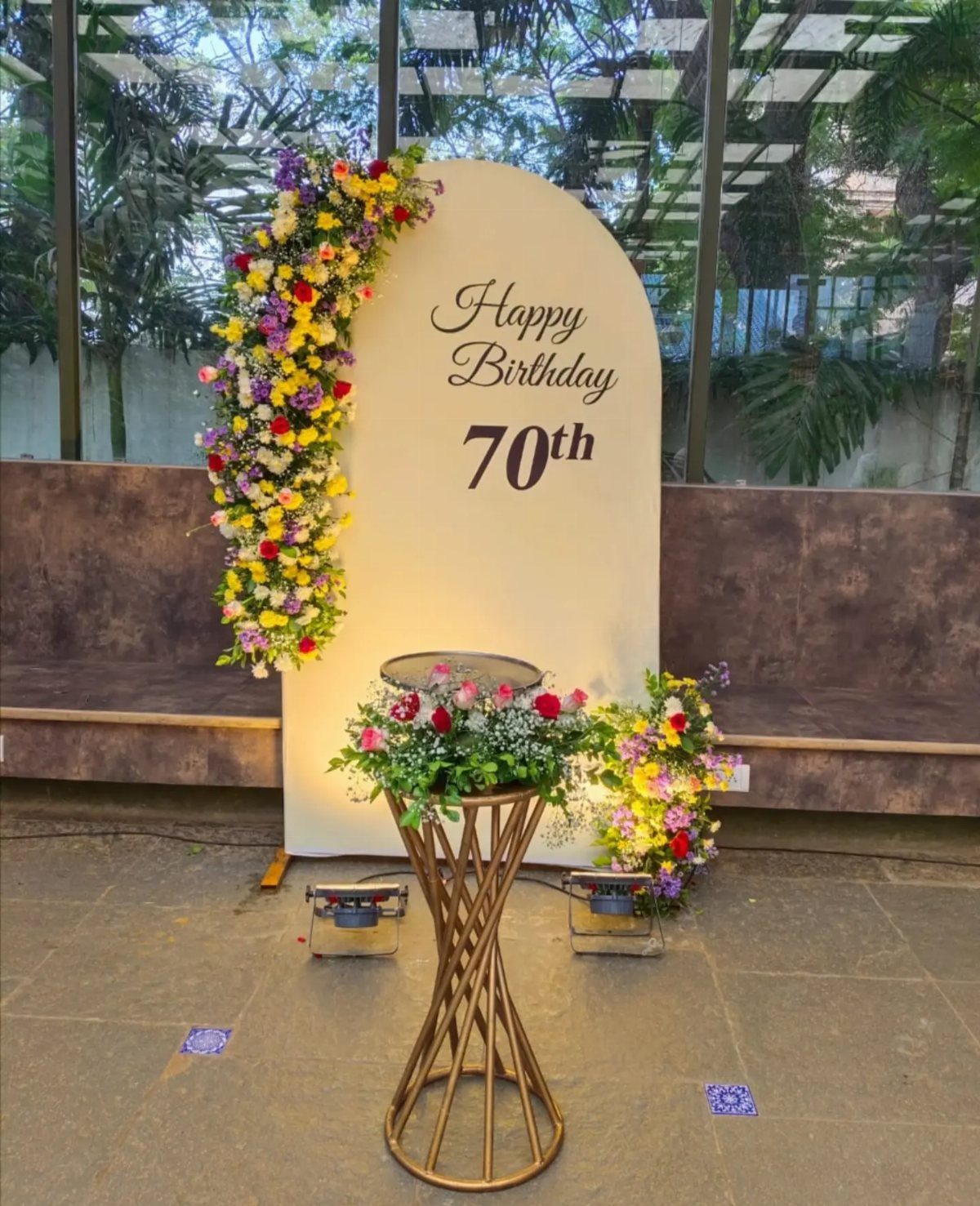 A white arched birthday backdrop with colorful flowers and Happy Birthday 70th text.